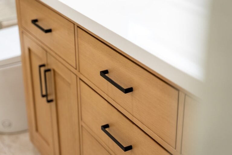 Close-up of natural wood shaker vanity cabinets with matte black bar pulls and white countertop by RnD Builders Inc
