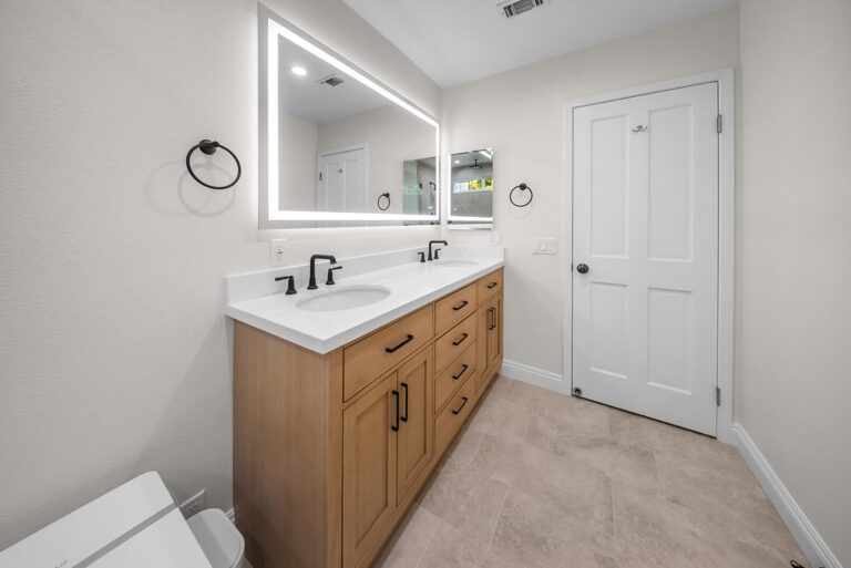 Agoura Hills bathroom remodel: Double-sink bathroom vanity with warm wood cabinets, white quartz countertop, and LED mirror in Agoura Hills by RnD Builders Inc
