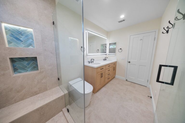 Modern master bathroom with glass shower enclosure, blue herringbone tile niches, and light wood double vanity by RnD Builders Inc