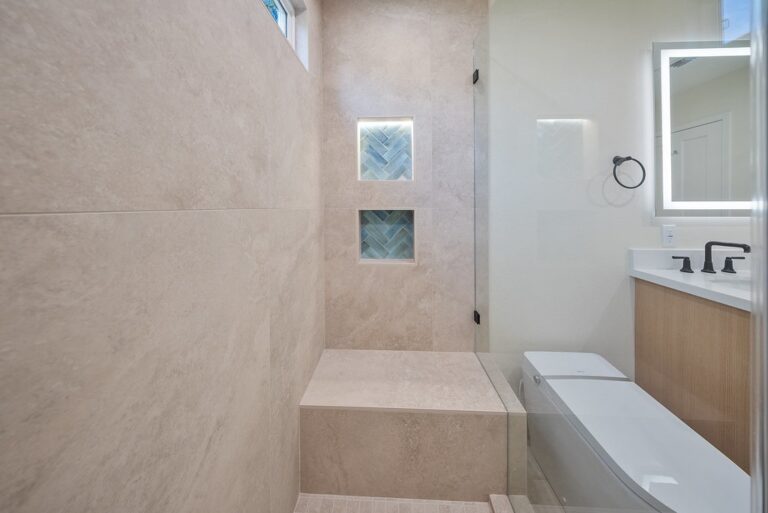 Modern walk-in shower with large format beige tile, built-in bench, and herringbone niche accents by RnD Builders Inc