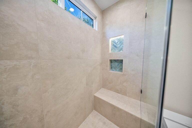 Agoura Hills bathroom remodel: Large-format beige tile walk-in shower with built-in bench, herringbone niches, and frameless glass door in Agoura Hills by RnD Builders Inc