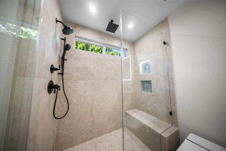 Walk-in shower with large format beige tile, matte black fixtures, and frameless glass enclosure by RnD Builders Inc