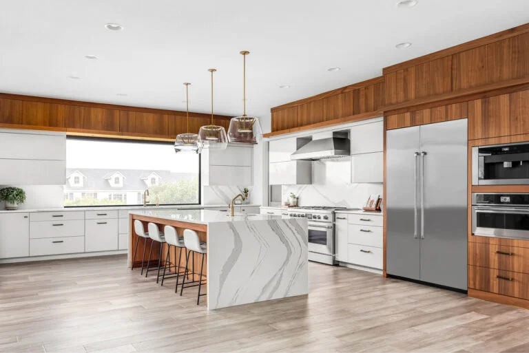 Contemporary kitchen with waterfall quartz island, walnut upper cabinets, and stainless steel appliances by RnD Builders Inc