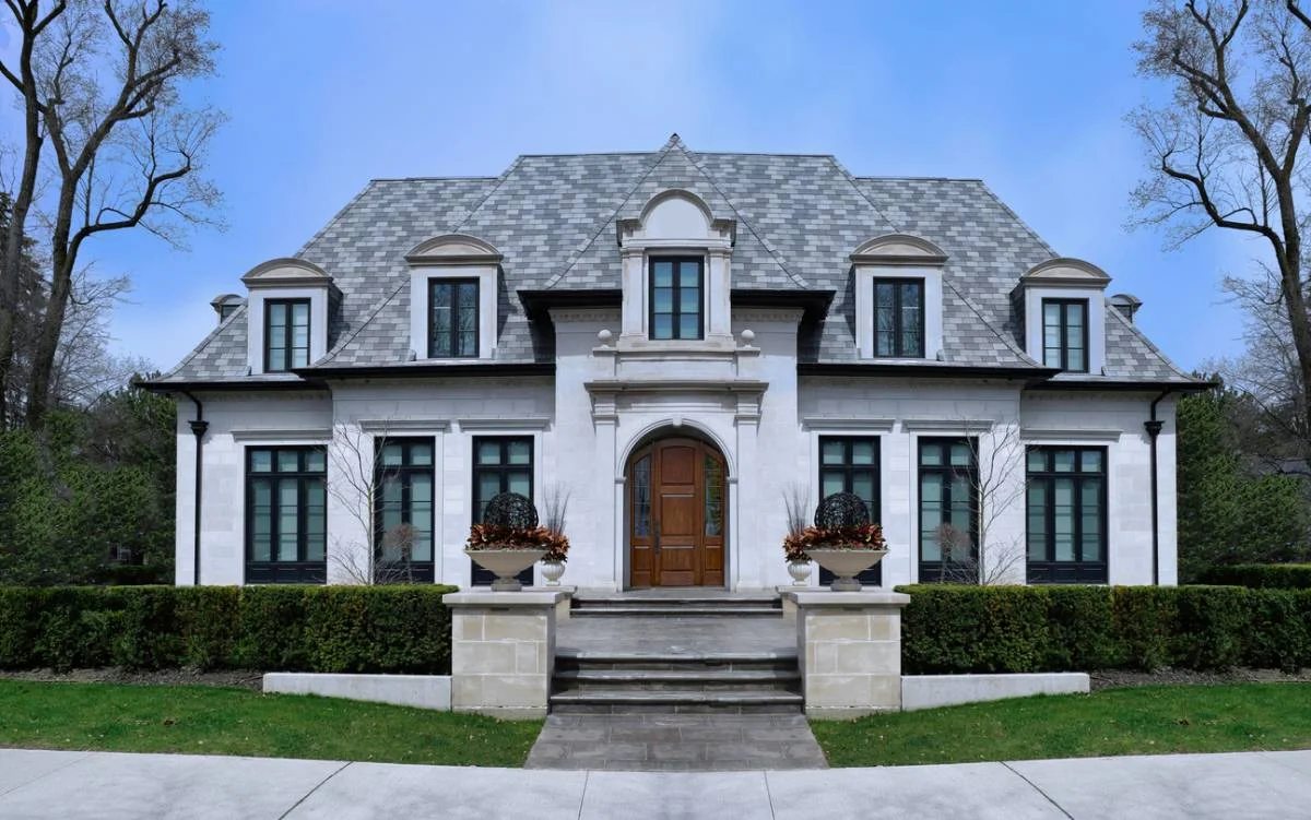 French château-style luxury home with limestone facade, slate roof, and arched wood entry door by RnD Builders Inc