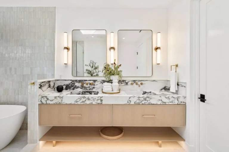 Luxury primary bathroom with floating oak vanity, dramatic veined marble countertop, and brass sconces by RnD Builders Inc