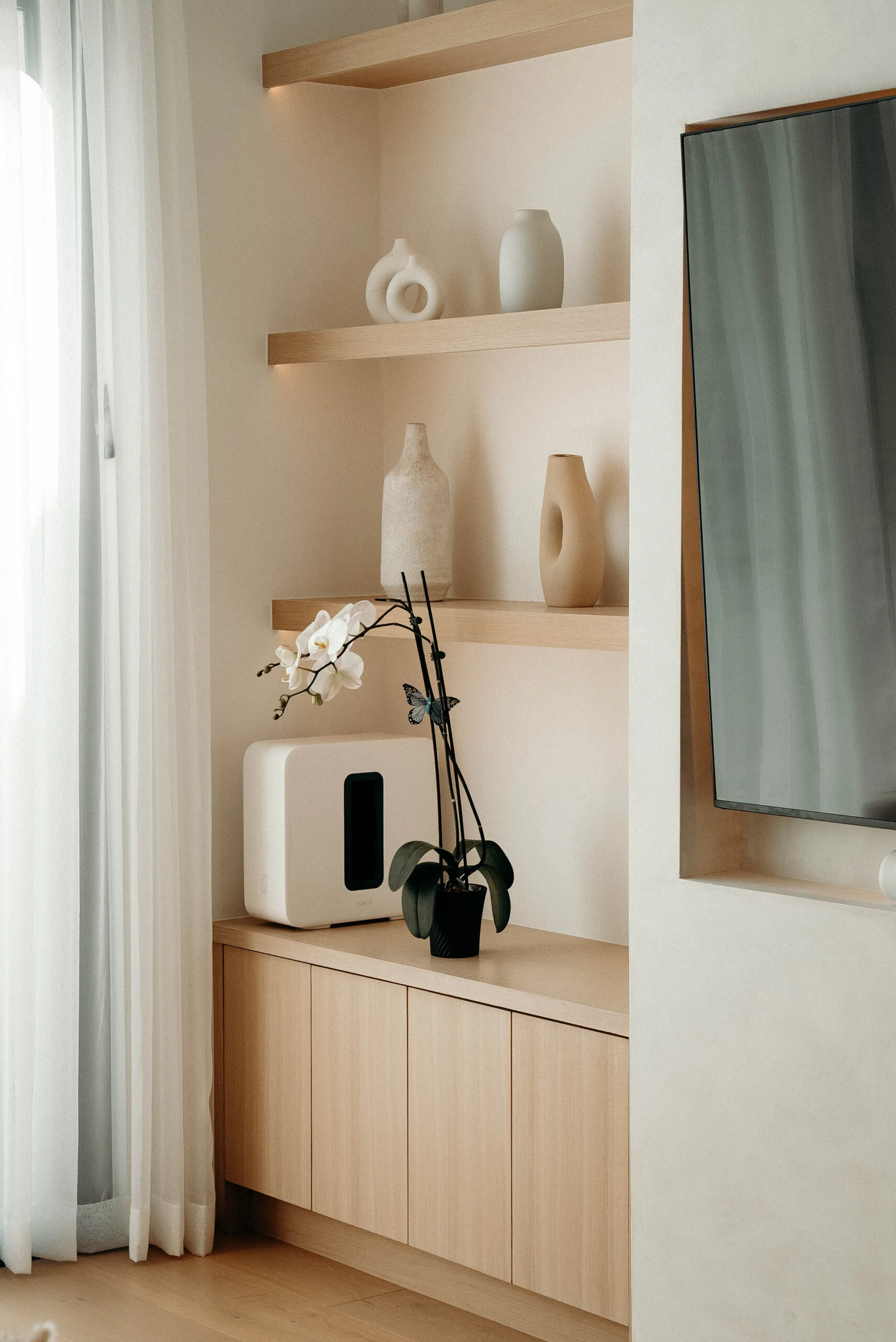 Built-in light oak floating shelves and lower cabinet unit in a minimalist living room by RnD Builders Inc