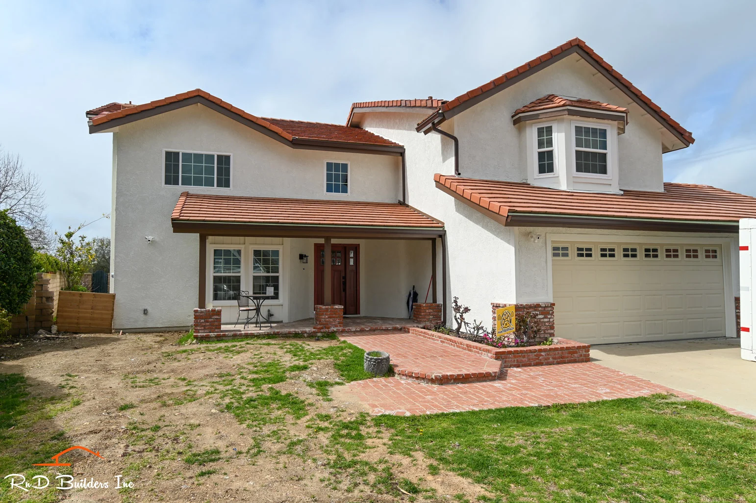 Two-story stucco home with red clay tile roof, brick walkway, and two-car garage by RnD Builders Inc
