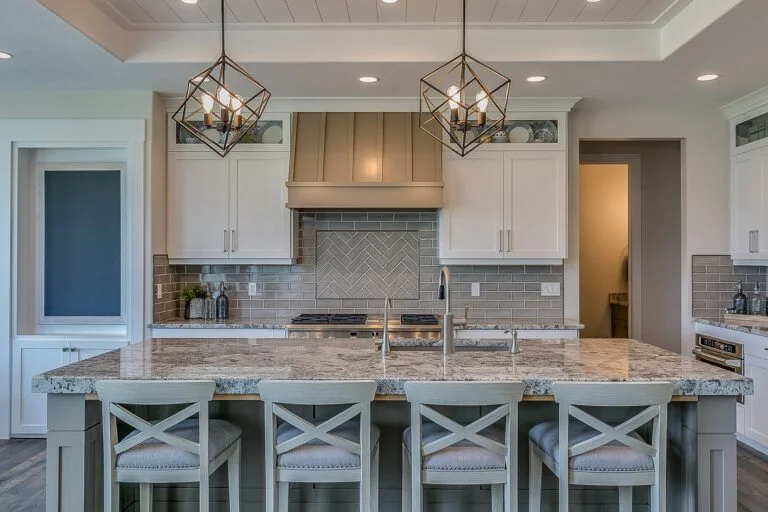 Transitional white kitchen with granite island, gray subway tile backsplash, and geometric pendant lights by RnD Builders Inc