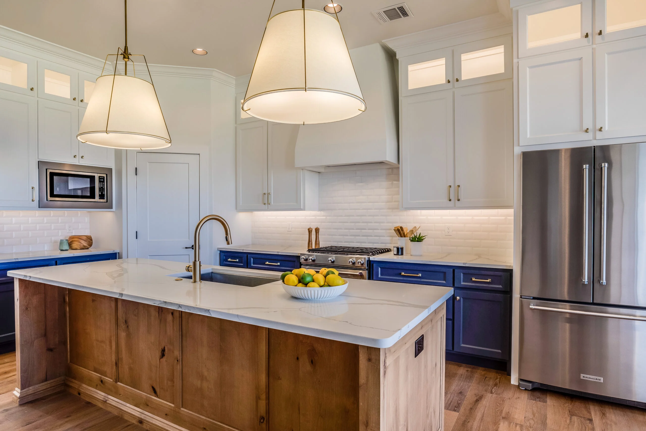 Transitional kitchen with navy lower cabinets, knotty alder island, quartz countertops, and drum pendant lights by RnD Builders Inc