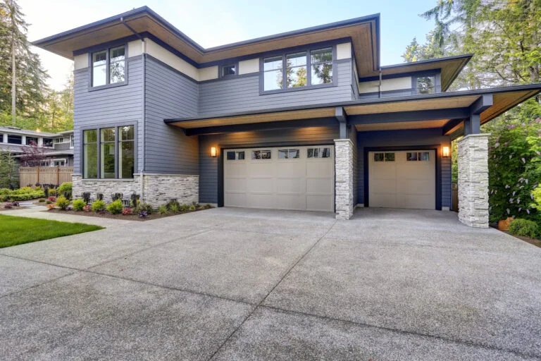 Two-story modern home with gray lap siding, stacked stone accents, and three-car garage by RnD Builders Inc