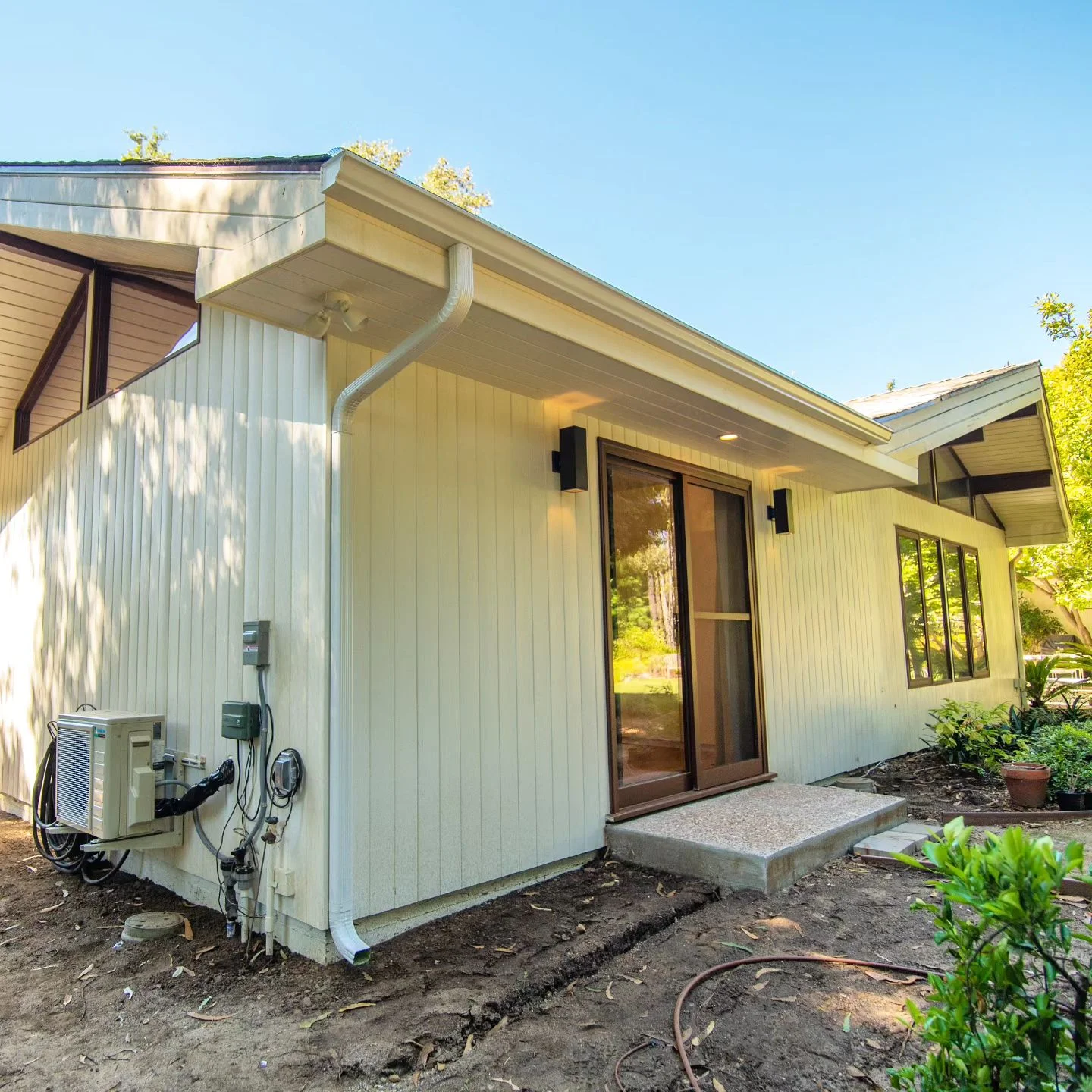 Exterior of single-story home with vertical board siding, sliding glass door, and mini-split HVAC unit by RnD Builders Inc