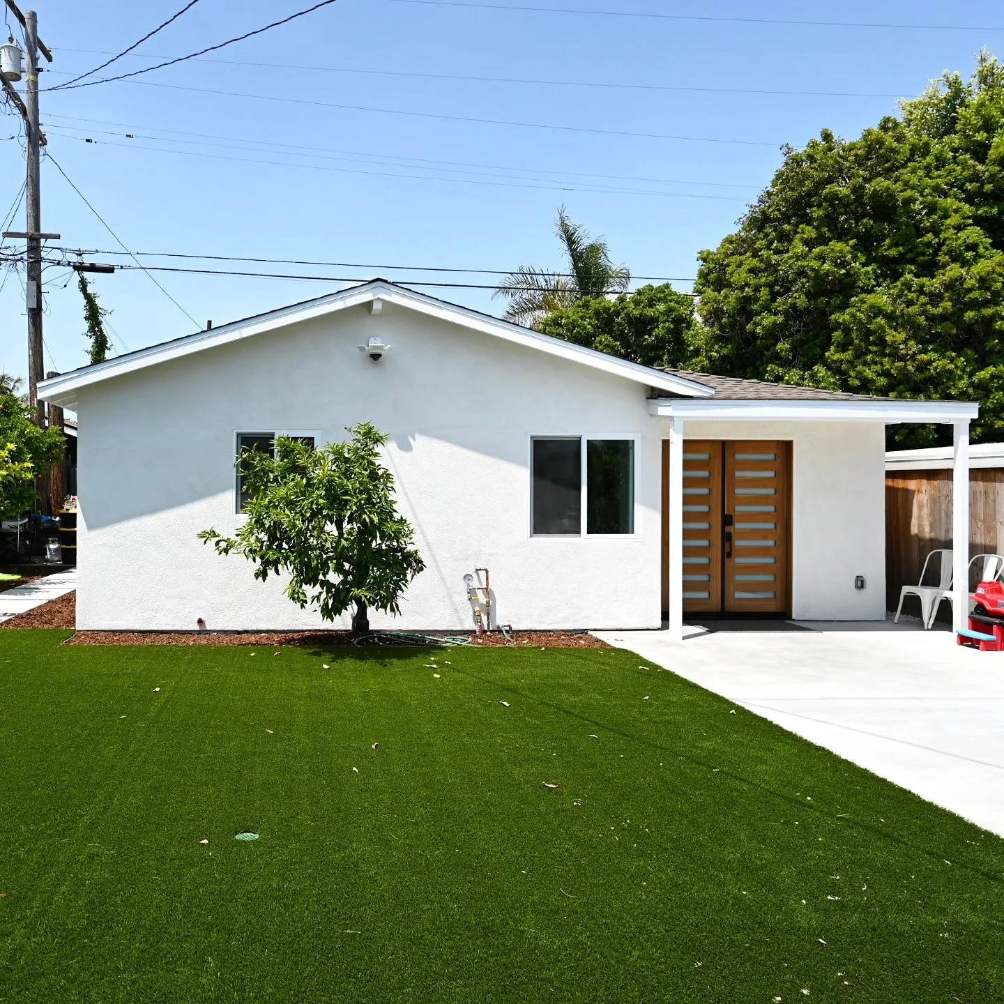 Single-story white stucco home with modern wood double entry door and artificial turf front yard by RnD Builders Inc