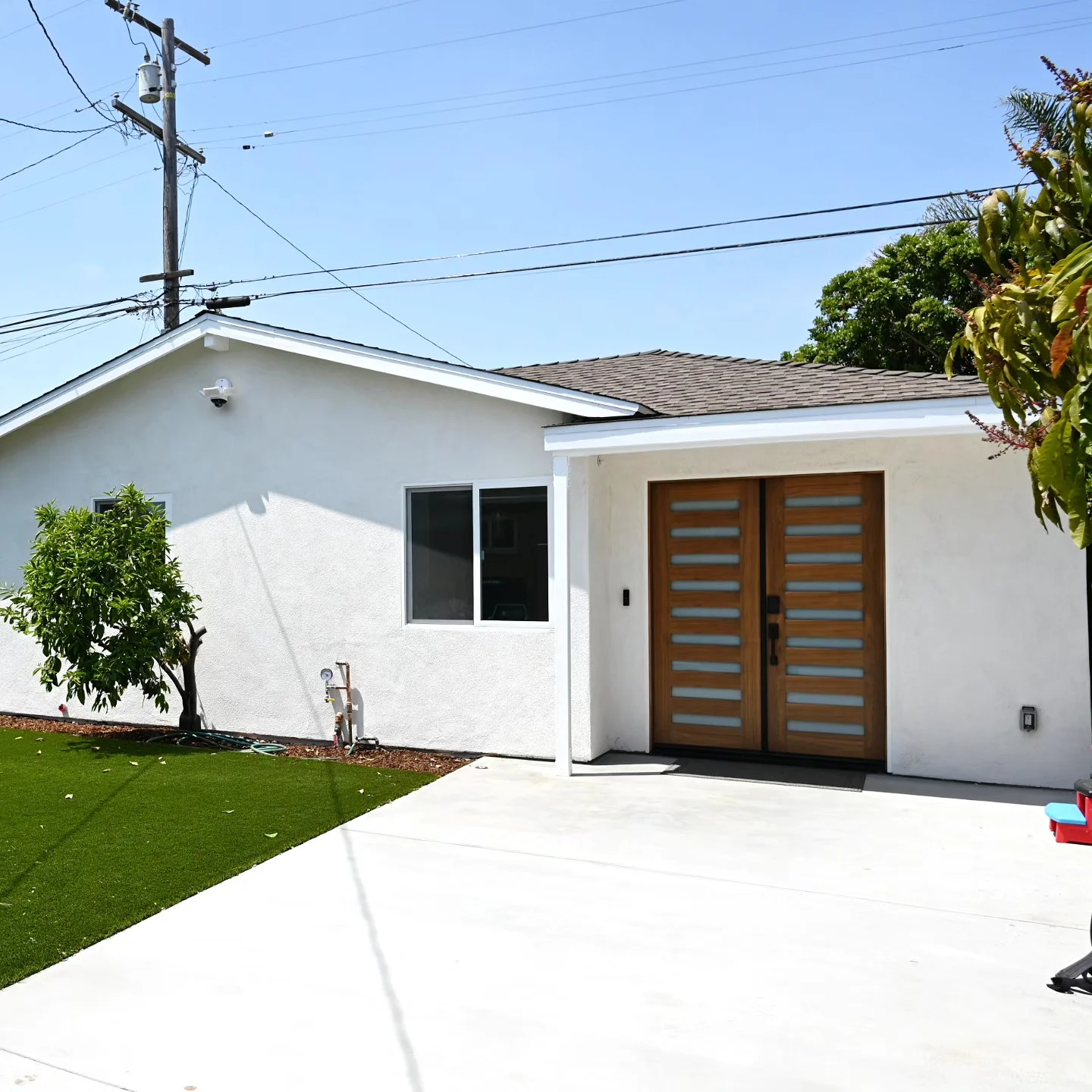 Single-story white stucco home with modern wood and frosted glass double entry doors by RnD Builders Inc