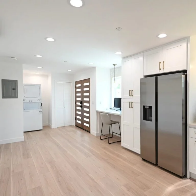 Open kitchen and utility area with white shaker cabinets, stainless steel refrigerator, and light hardwood floors by RnD Builders Inc