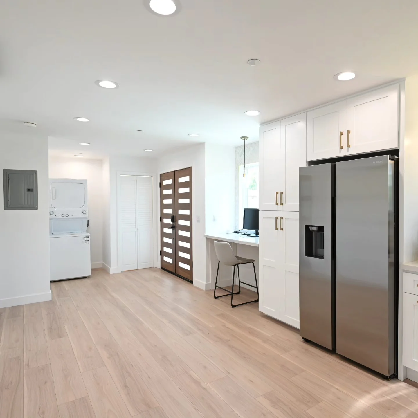 Open kitchen and utility area with white shaker cabinets, stainless steel refrigerator, and light hardwood floors by RnD Builders Inc
