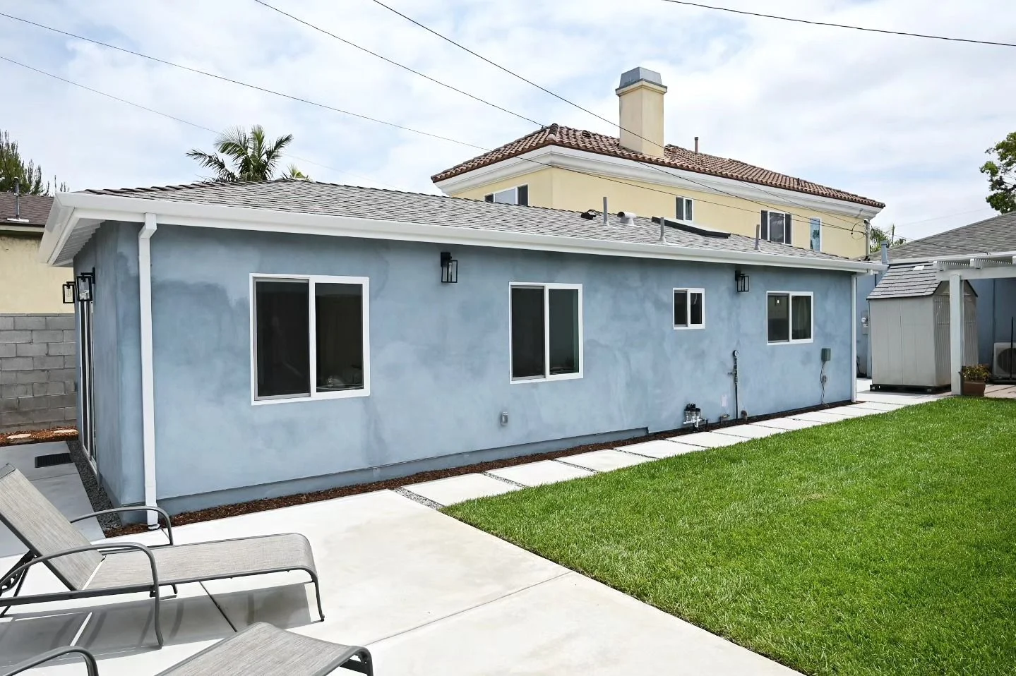 Rear exterior of newly constructed ADU with blue-gray stucco finish and white-trimmed windows by RnD Builders Inc