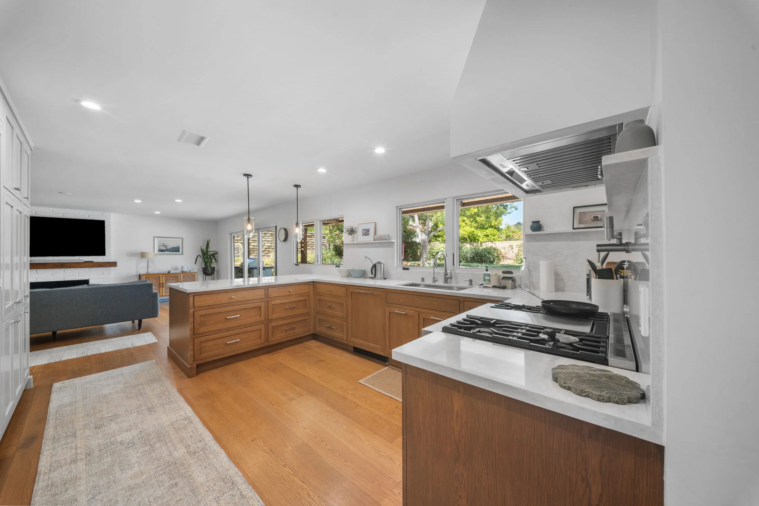 Open-concept kitchen with warm walnut shaker cabinets, white quartz countertops, and stainless gas cooktop by RnD Builders Inc