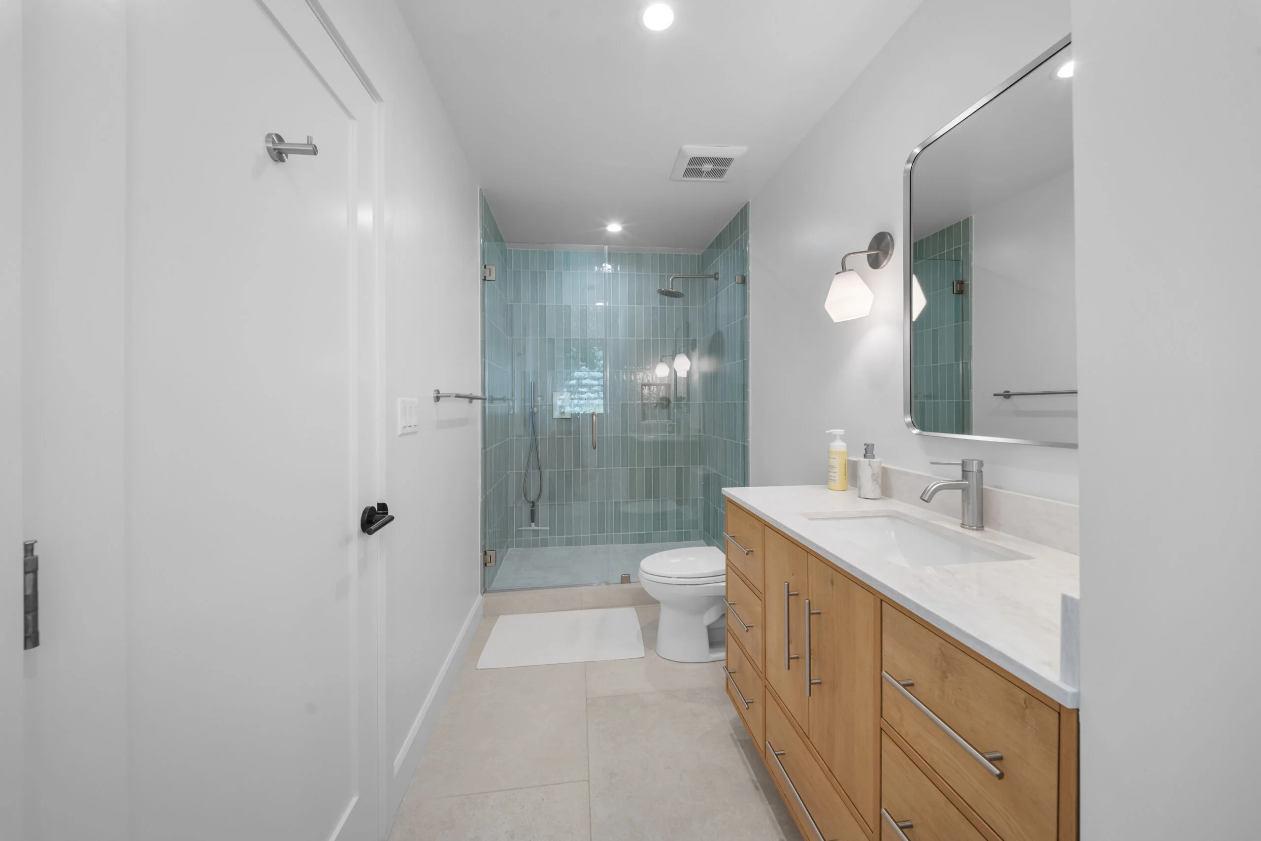 Modern full bathroom with teal vertical subway tile walk-in shower and natural wood vanity by RnD Builders Inc