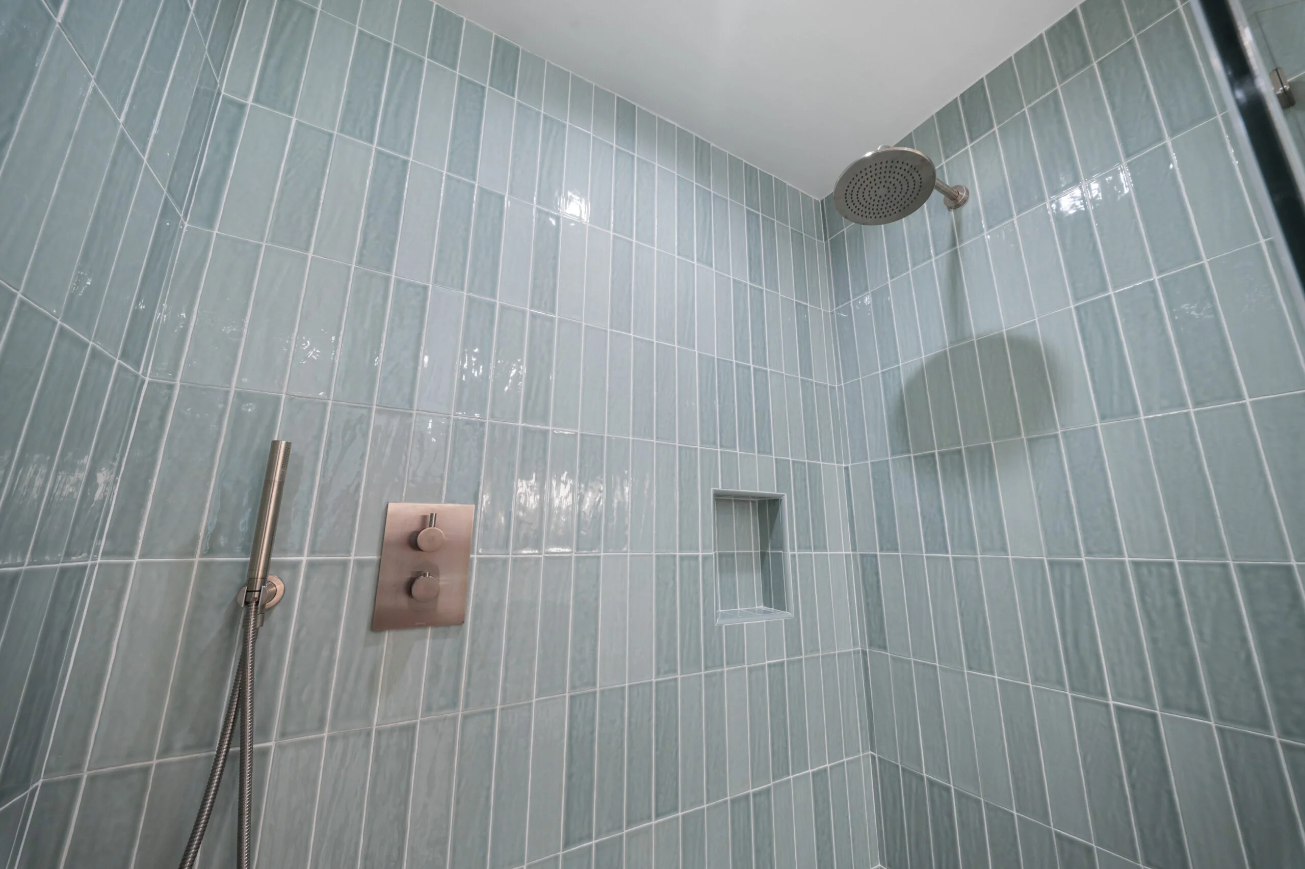 Walk-in shower with vertical seafoam green glass tile, brushed nickel rain showerhead and thermostatic valve by RnD Builders Inc