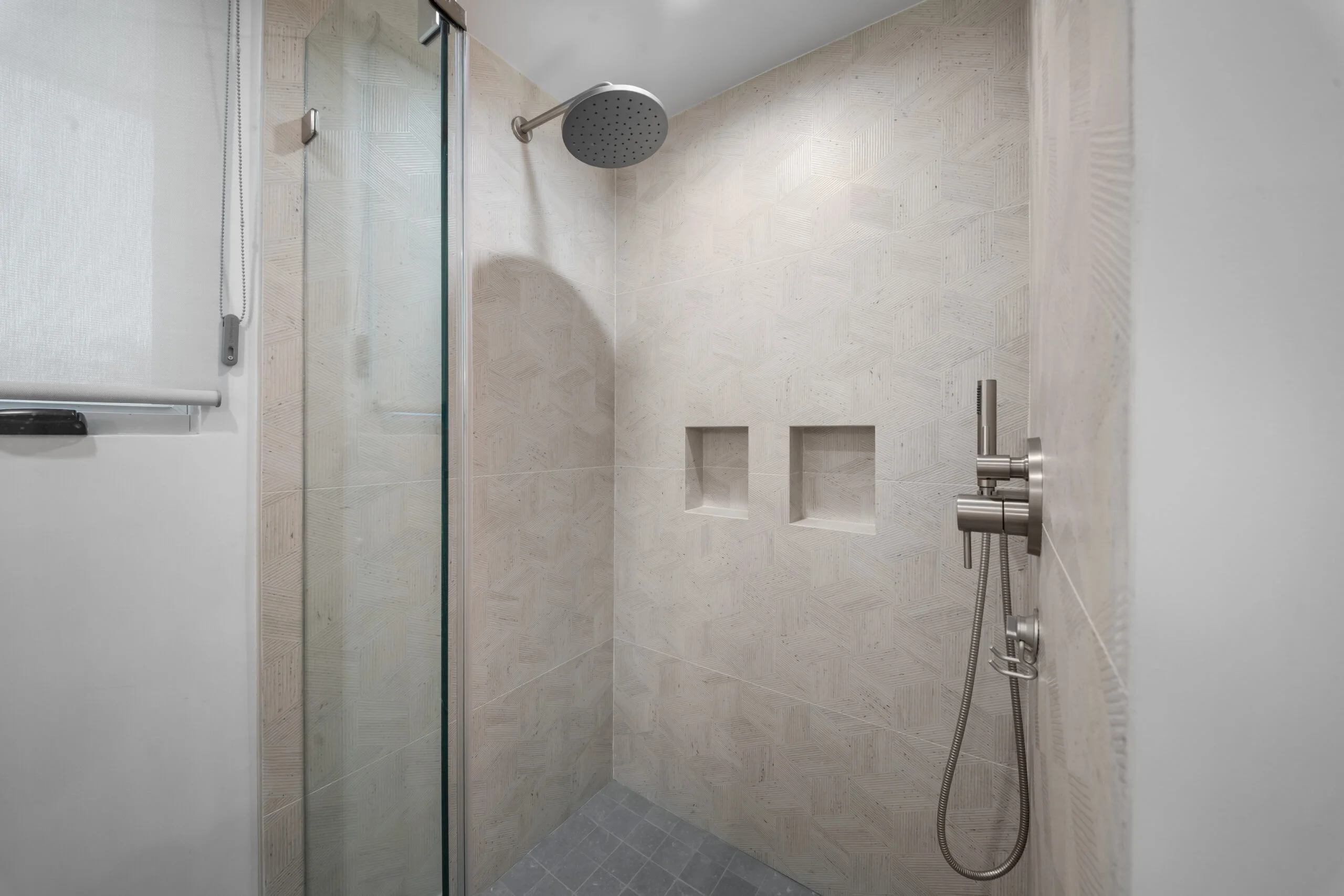 Walk-in shower with textured beige large-format tile, rain showerhead, and dual built-in niches by RnD Builders Inc