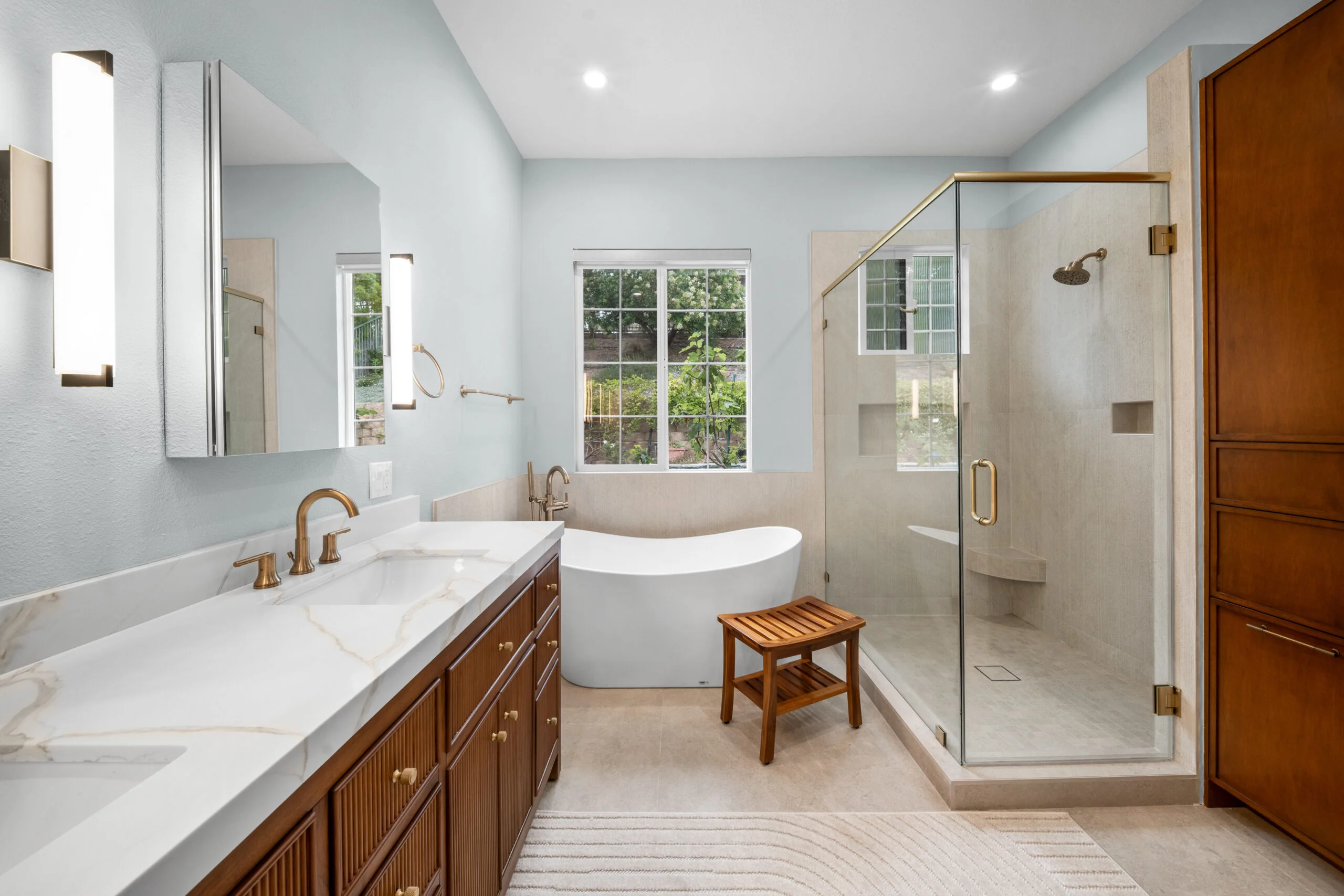 Luxury primary bathroom with freestanding soaking tub, glass shower enclosure, and walnut double vanity by RnD Builders Inc
