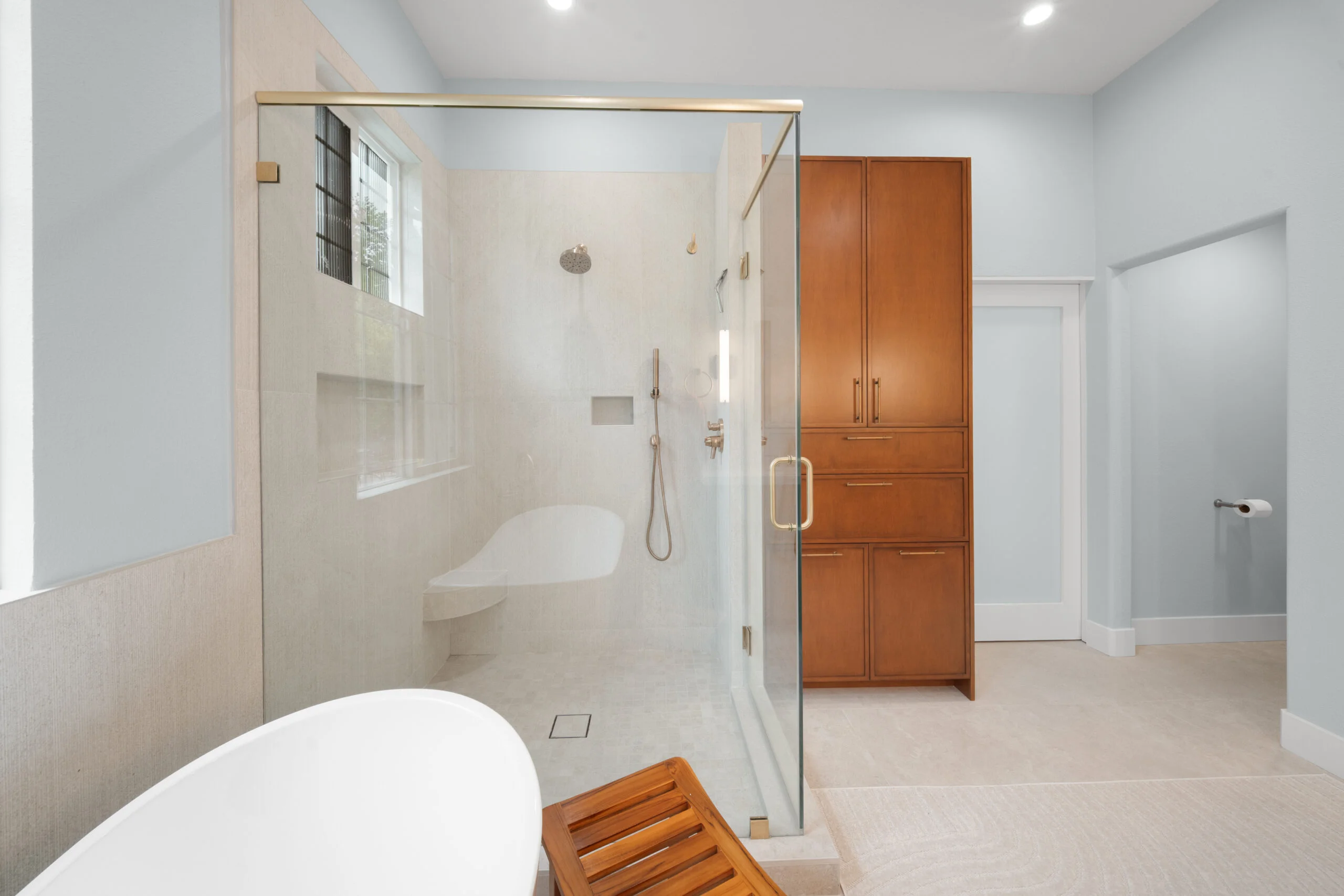 Luxury master bathroom with glass shower enclosure, freestanding tub, and warm wood cabinetry by RnD Builders Inc
