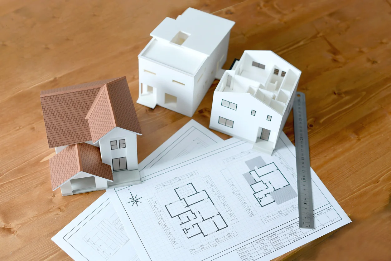Architectural scale models and floor plan blueprints with metal ruler on wood surface by RnD Builders Inc