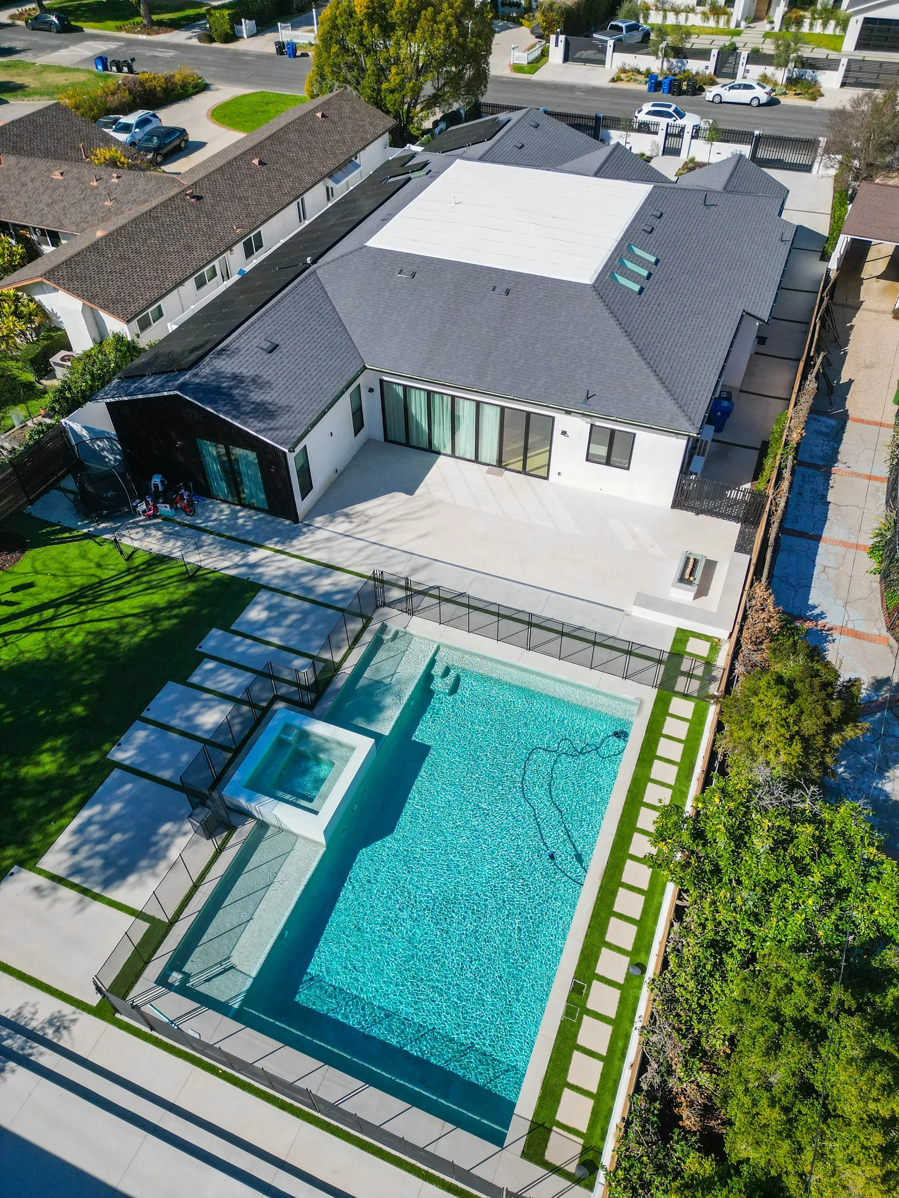 Aerial view of modern white stucco home with rectangular pool, spa, and concrete patio by RnD Builders Inc
