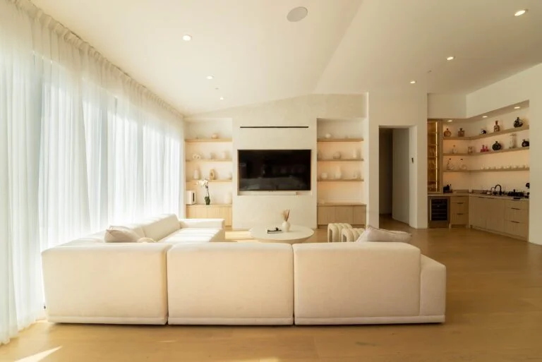 Bright open-concept living room with built-in shelving, wall-mounted TV, and white sectional sofa by RnD Builders Inc