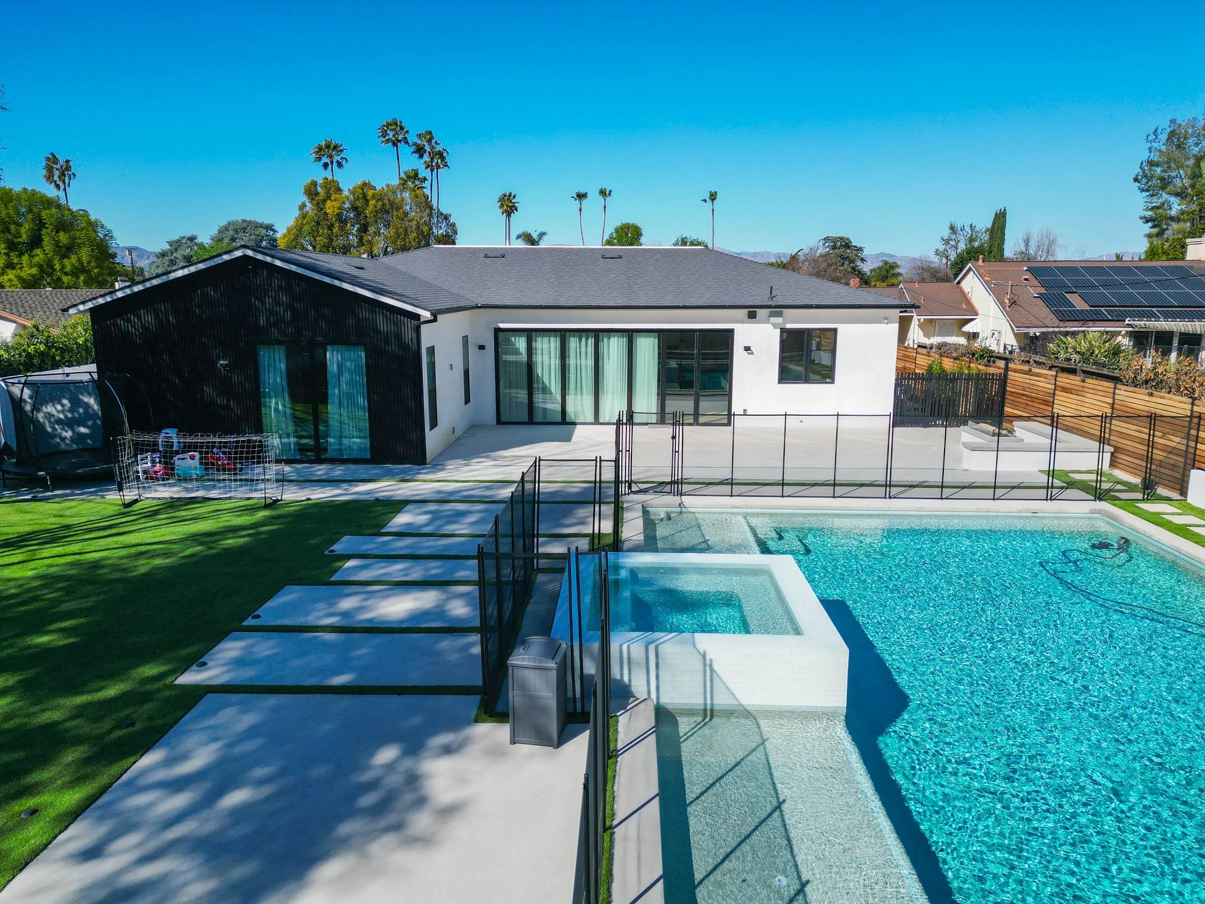 Modern white stucco home with large rectangular pool, spa, and artificial turf backyard by RnD Builders Inc