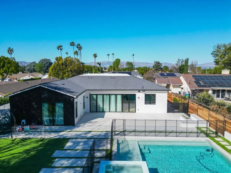 Aerial view of modern single-story home with pool, white stucco exterior, and black metal fence by RnD Builders Inc