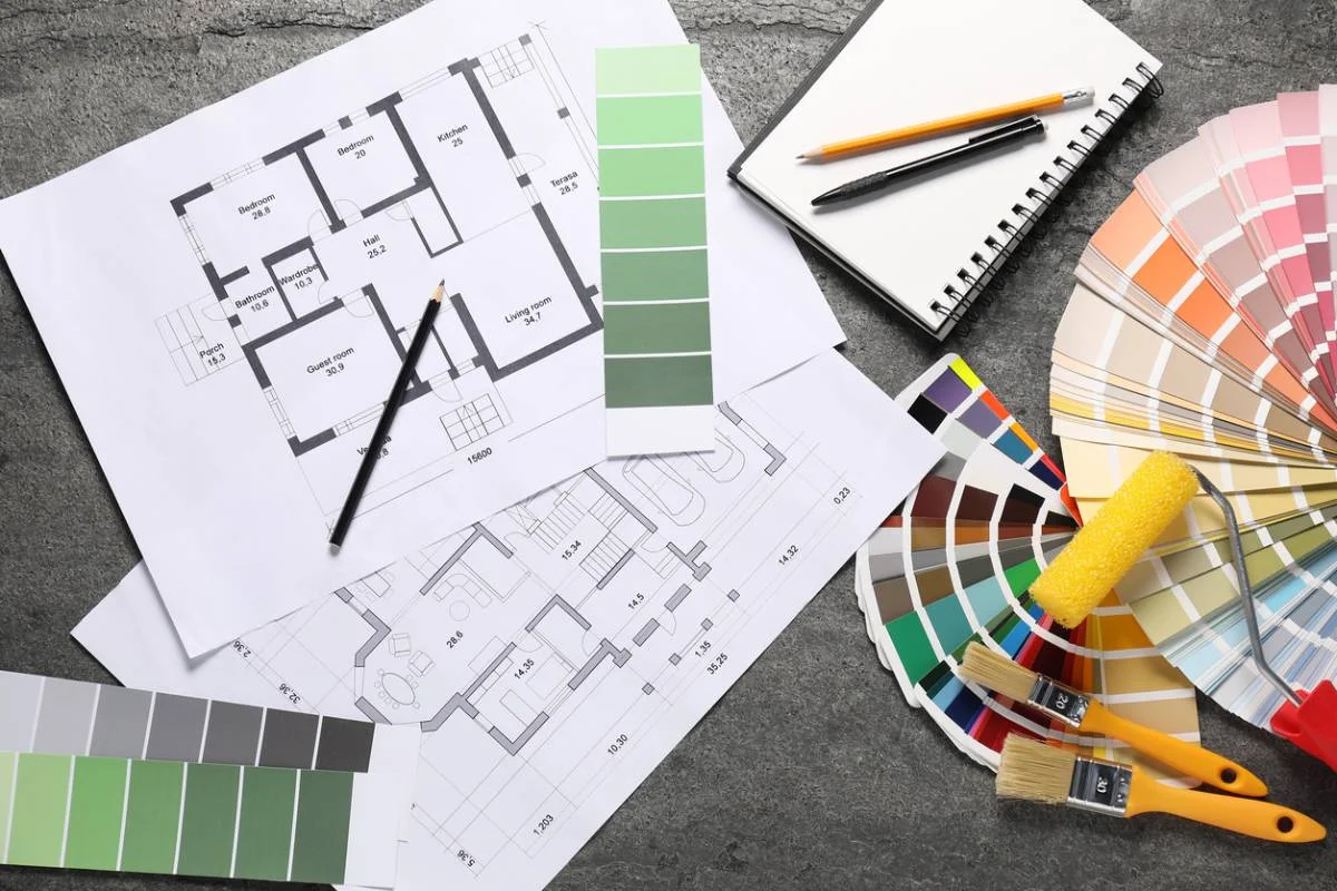 Residential floor plans, paint color swatches, brushes, roller, pencil, and notepad on gray surface by RnD Builders Inc