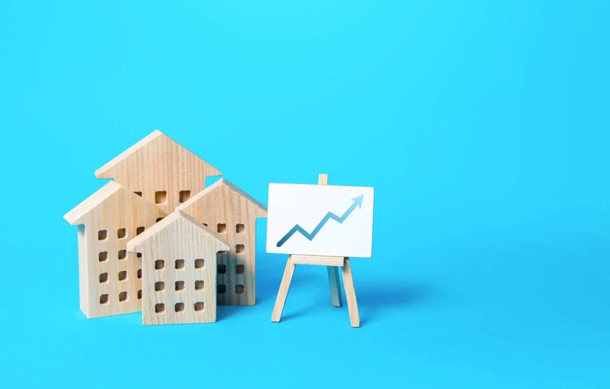 Decorative graphic image of wooden miniature house figurines and an easel displaying an upward trend arrow by RnD Builders Inc