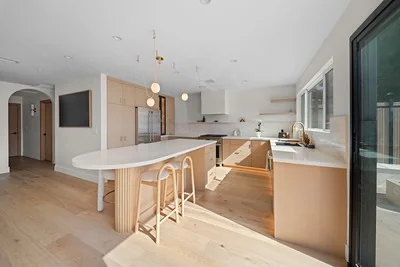 Open-concept kitchen with light wood flat-panel cabinets, oval island, and globe pendant lights by RnD Builders Inc