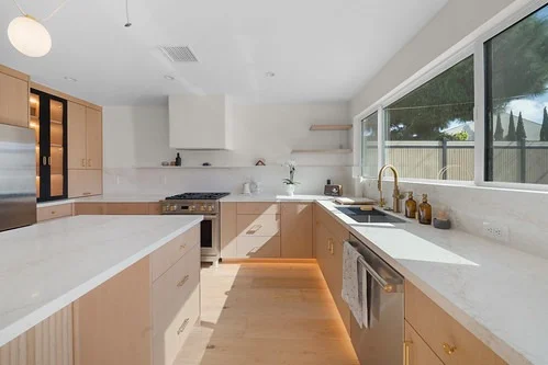 Bright modern kitchen with light wood flat-front cabinets, white quartz countertops, and under-cabinet LED lighting by RnD Builders Inc