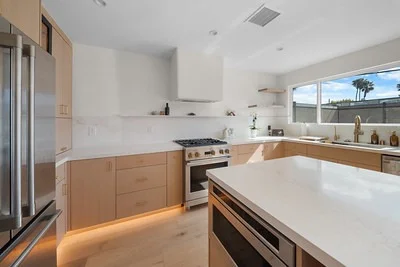 Modern kitchen with light wood flat-panel cabinets, white quartz countertops, and stainless steel appliances by RnD Builders Inc
