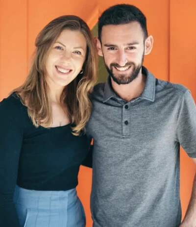 Two smiling team members posing together in front of an orange wall by RnD Builders Inc