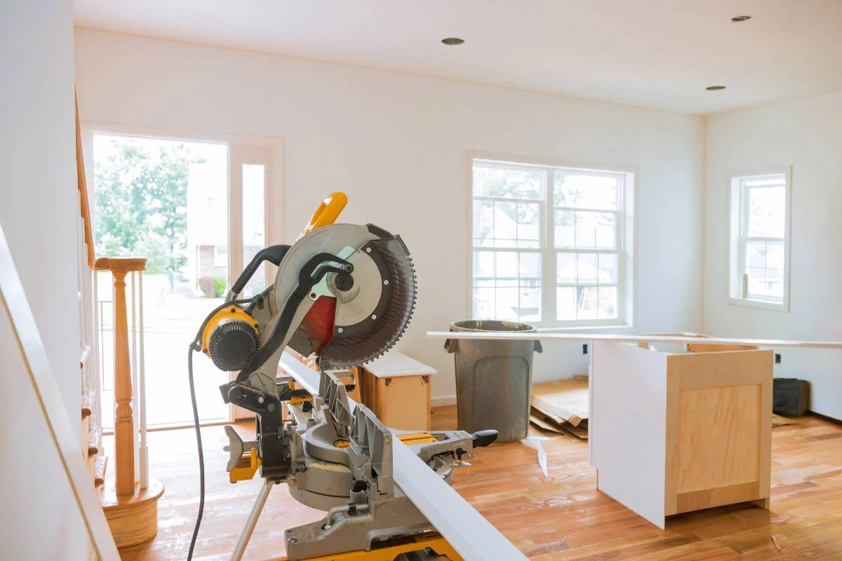 Miter saw and partially installed kitchen cabinets in an open-plan room under renovation by RnD Builders Inc