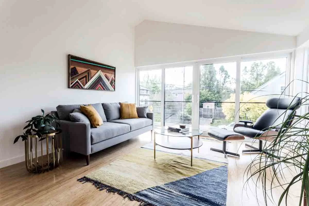 Bright mid-century modern living room with gray sofa, hardwood floors, and large sliding glass doors by RnD Builders Inc