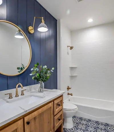 Farmhouse bathroom with navy shiplap accent wall, wood vanity, and patterned tile floor by RnD Builders Inc