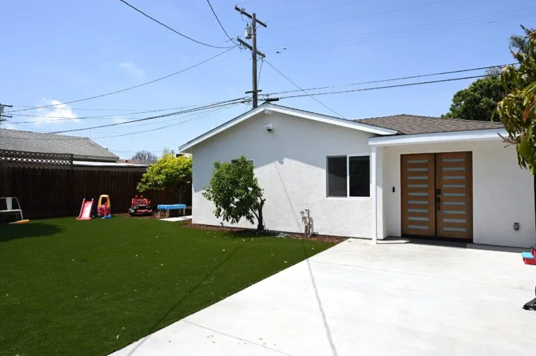 White stucco ADU exterior with modern wood double entry door and artificial turf backyard by RnD Builders Inc