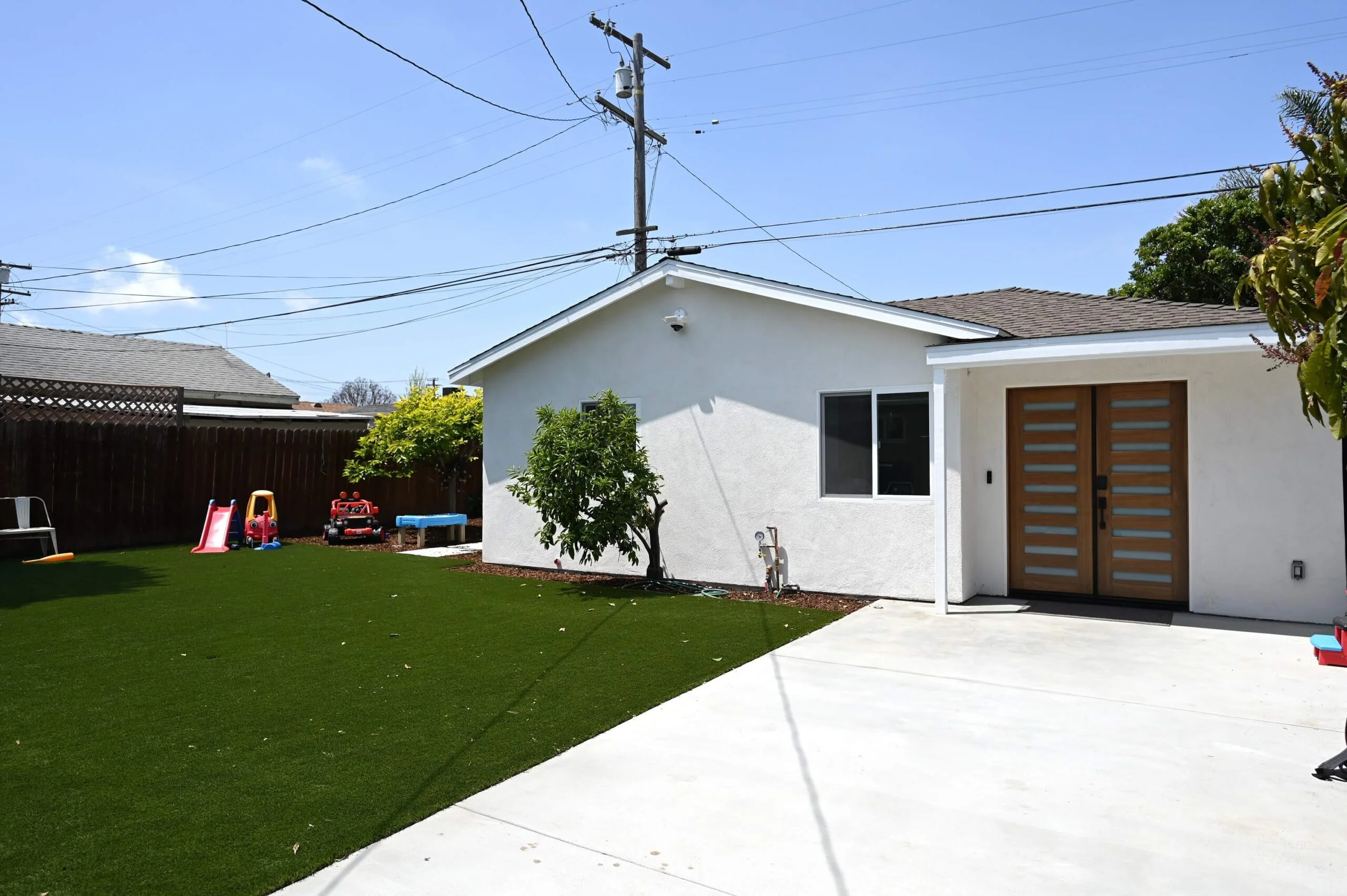 White stucco ADU exterior with modern wood double entry door and artificial turf backyard by RnD Builders Inc