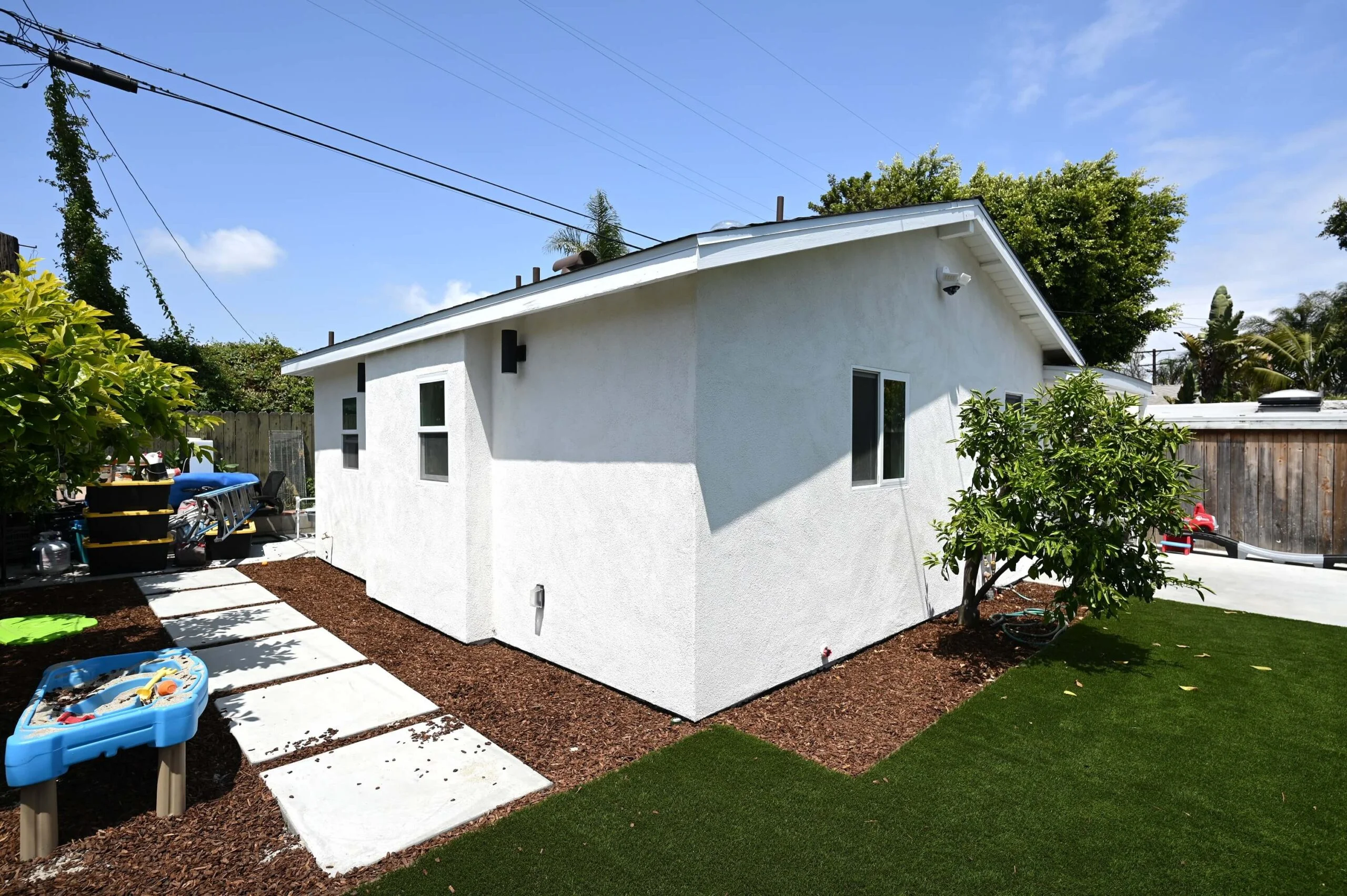 White stucco ADU with pitched roof, modern windows, and landscaped backyard by RnD Builders Inc