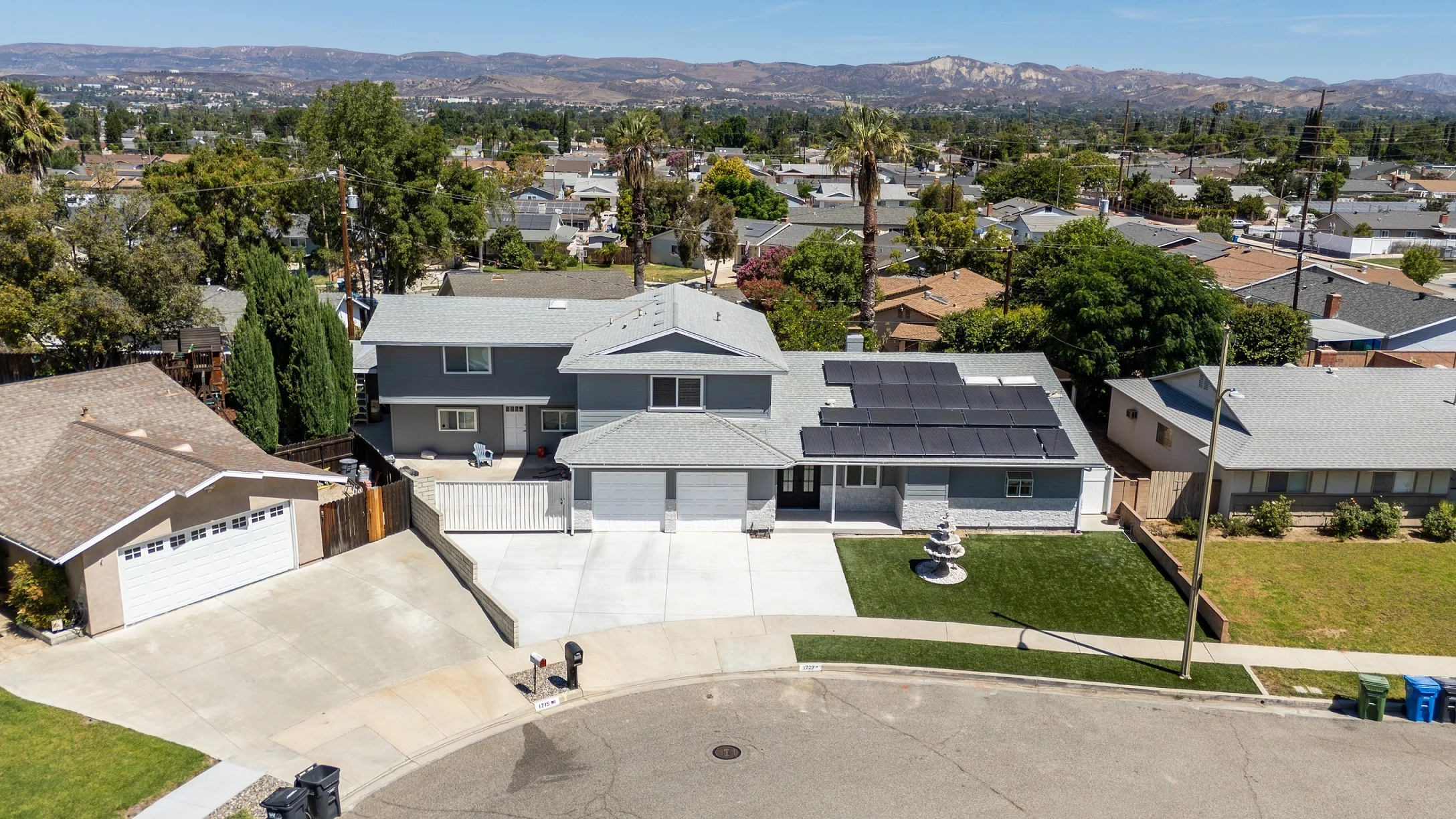 Aerial view of two-story gray residential home with solar panels, three-car garage, and mountain backdrop by RnD Builders Inc