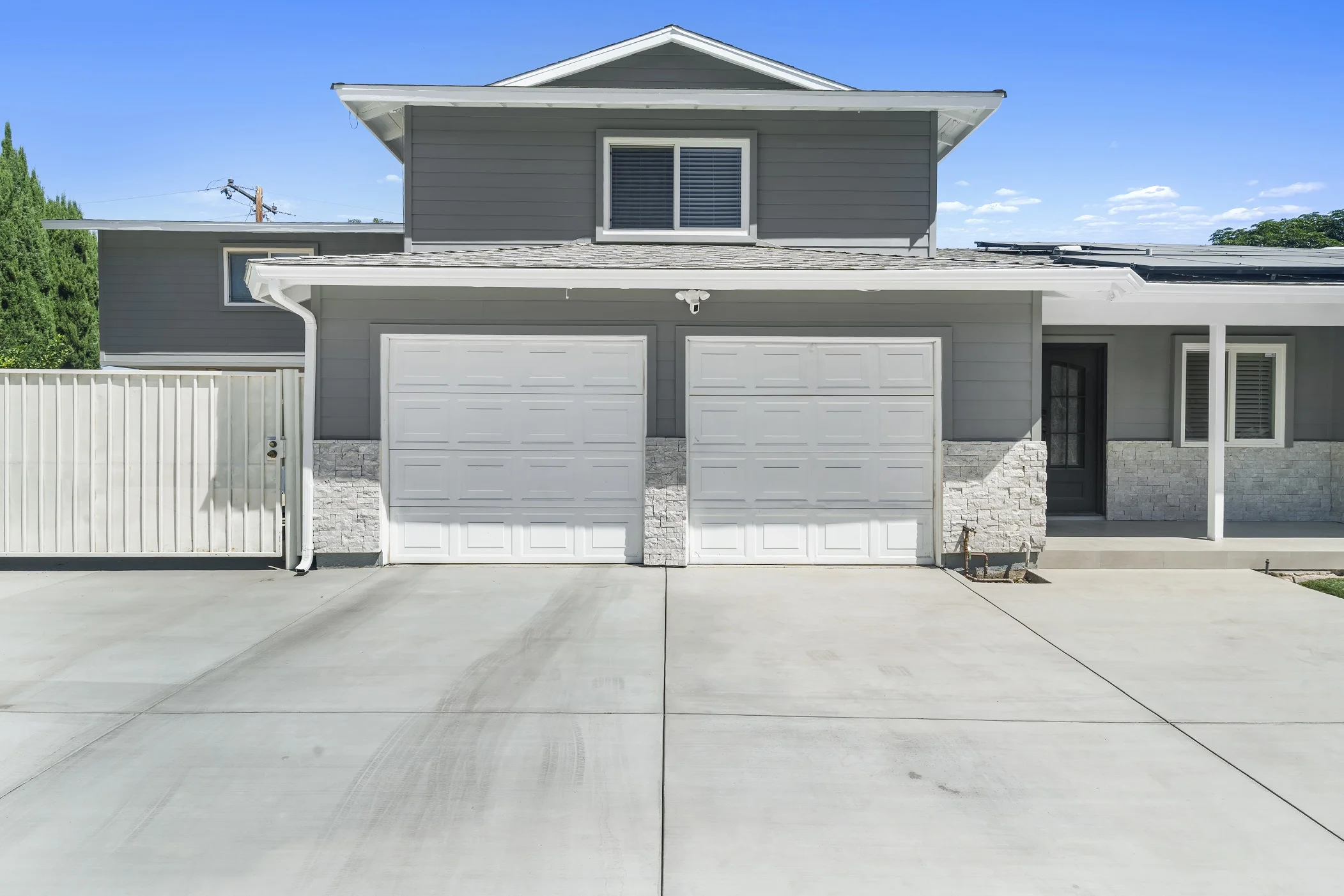 Two-story gray home exterior with dual white garage doors and stacked stone veneer wainscoting by RnD Builders Inc