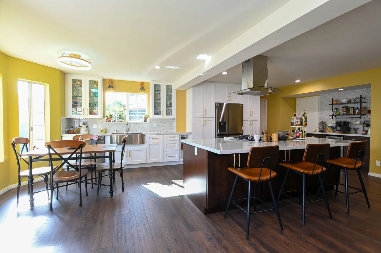 Open-concept kitchen with white shaker cabinets, dark walnut island, and yellow accent walls by RnD Builders Inc