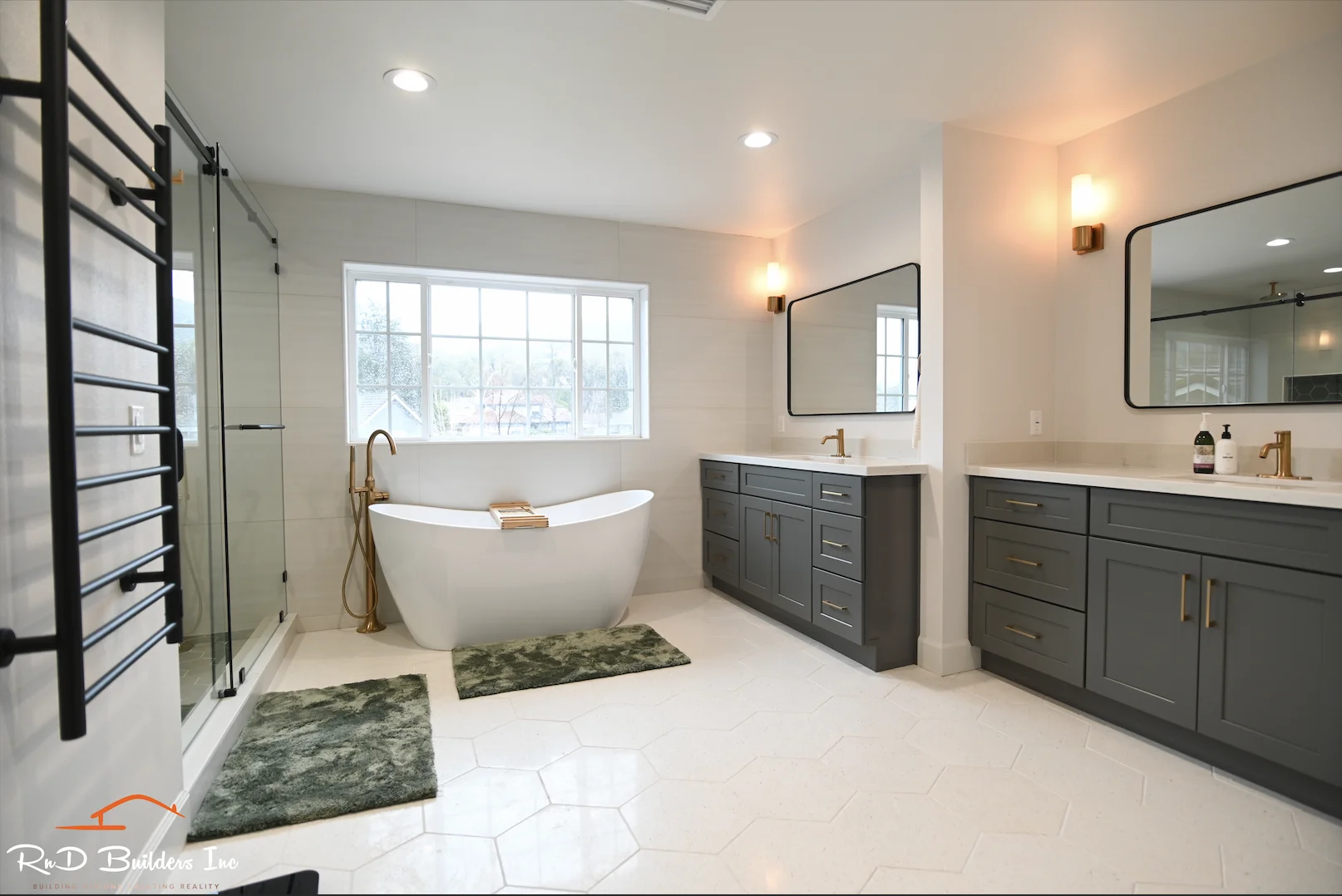 Luxury master bathroom with freestanding soaking tub, gray shaker vanities, and hexagon floor tile by RnD Builders Inc