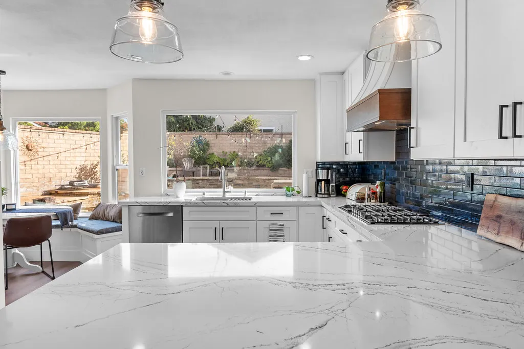 White shaker kitchen with marble quartz island, navy subway tile backsplash, and glass pendants by RnD Builders Inc