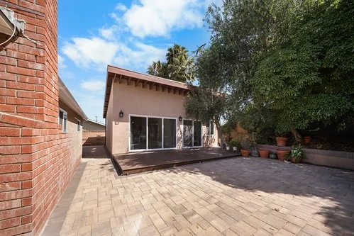 Backyard ADU with sliding glass doors, wood deck, and paver patio by RnD Builders Inc