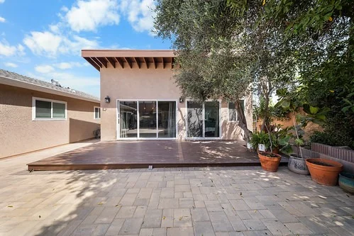 Rear exterior of two-story stucco home with wood deck and sliding glass doors by RnD Builders Inc